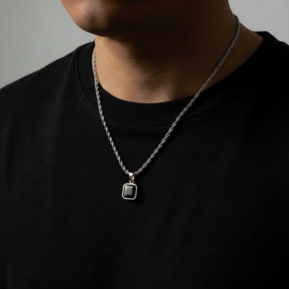 Person wearing a silver necklace with a black pendant on a plain background