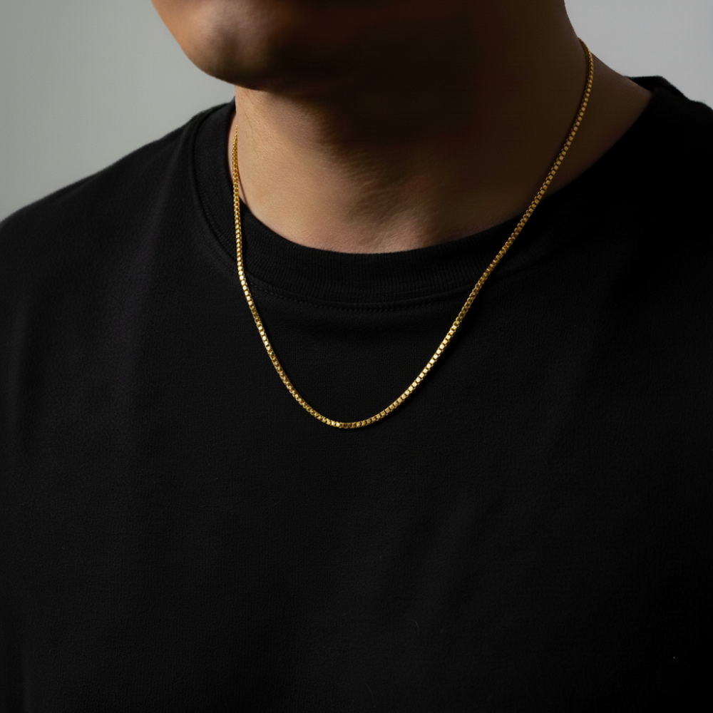 Person wearing a gold box chain necklace against a dark background
