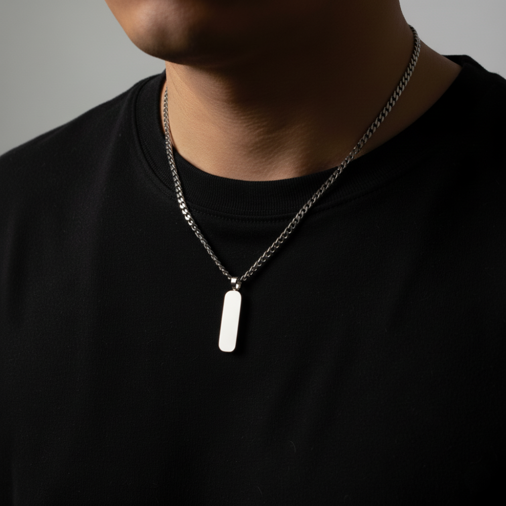 Person wearing a black shirt with a necklace featuring a chain with pendant against a neutral background