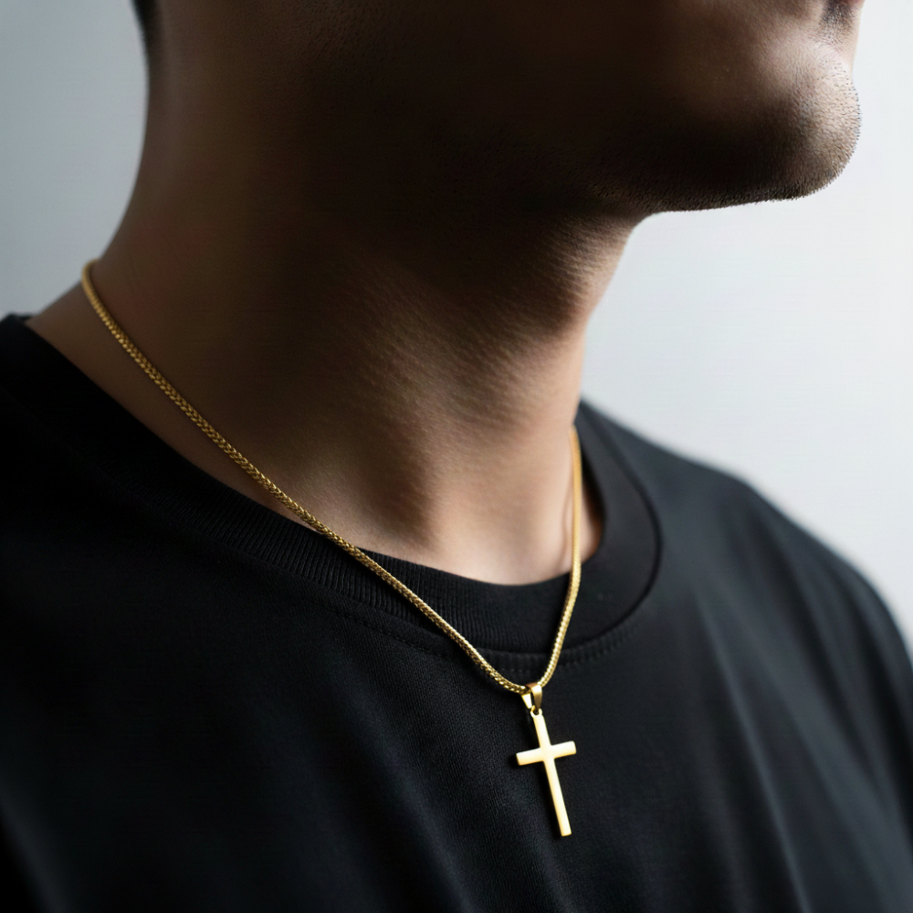 Person wearing a gold necklace with a cross pendant on a plain background