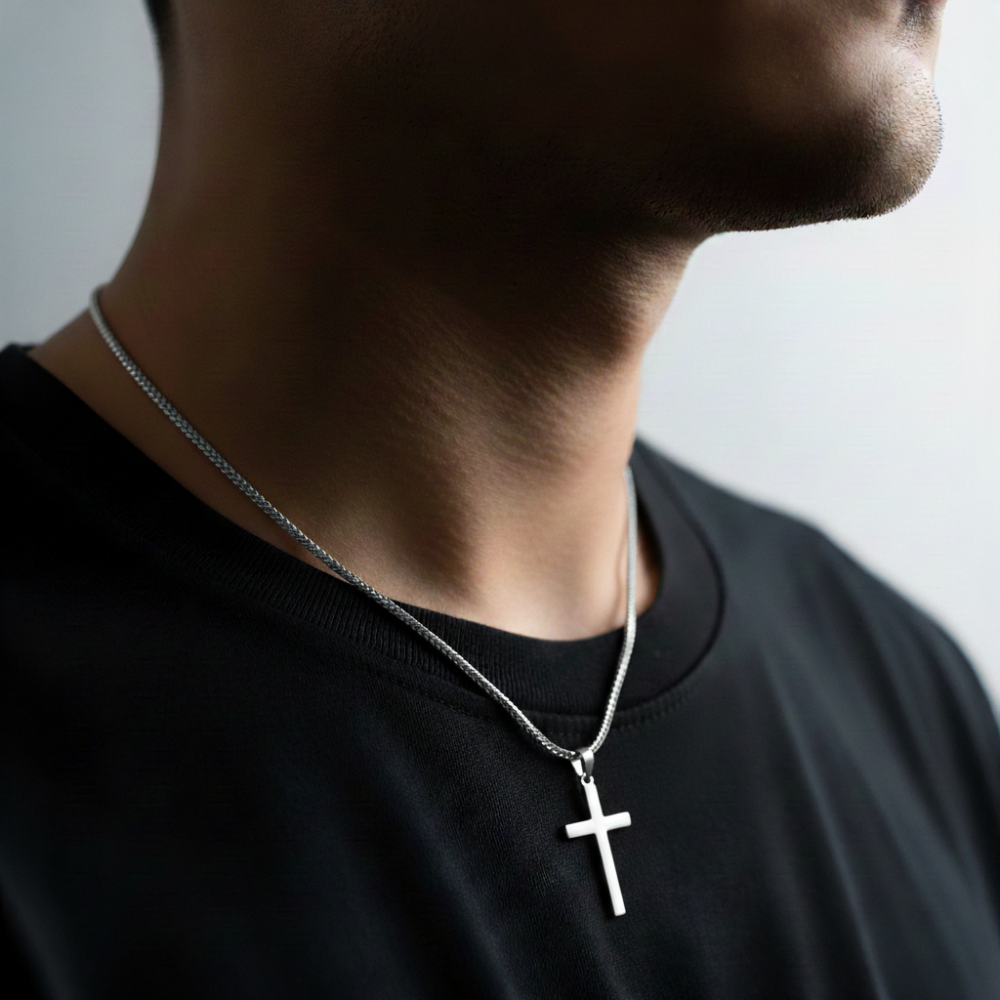 Person wearing a black shirt with a silver cross necklace against a neutral background