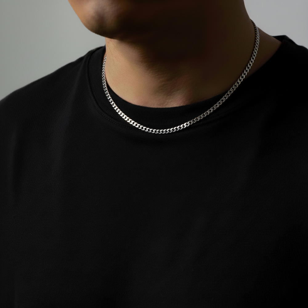 Person wearing a silver cuban chain necklace against a neutral background