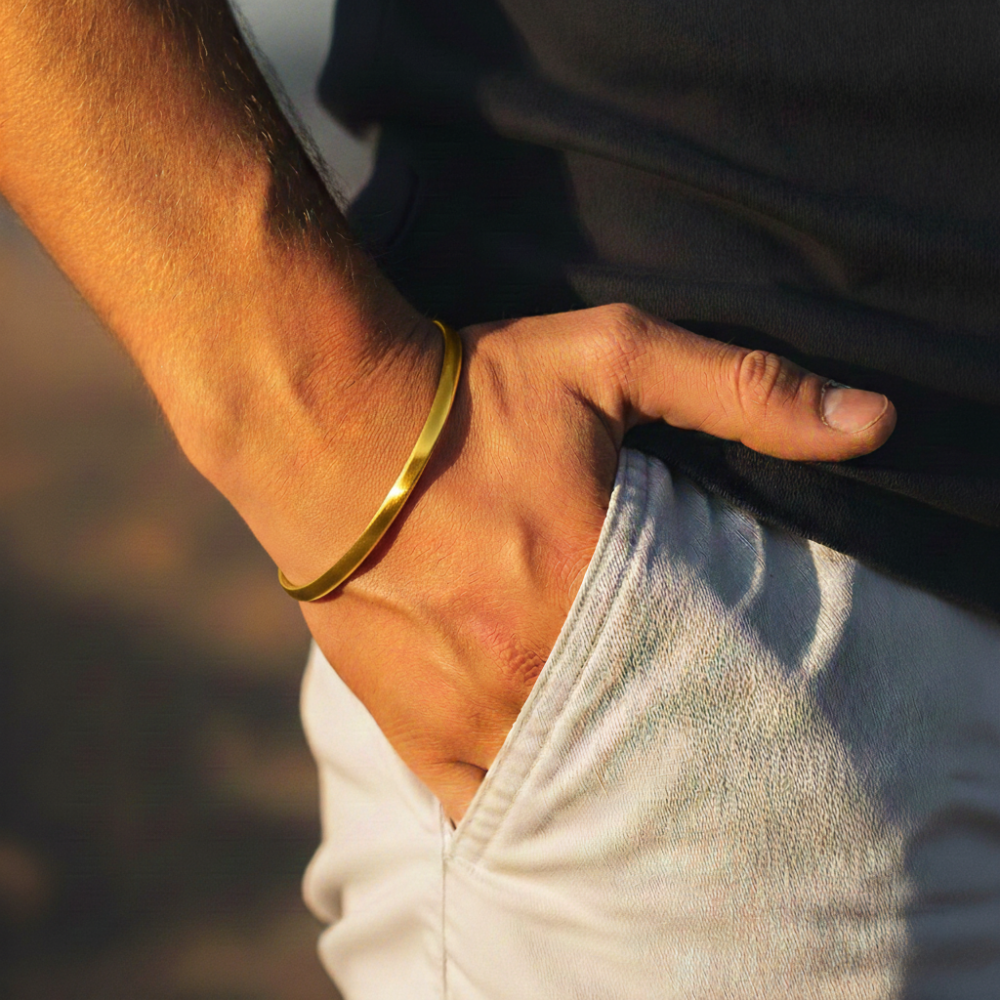 Close-up of a person's arm wearing a gold cuff bracelet with a blurred background