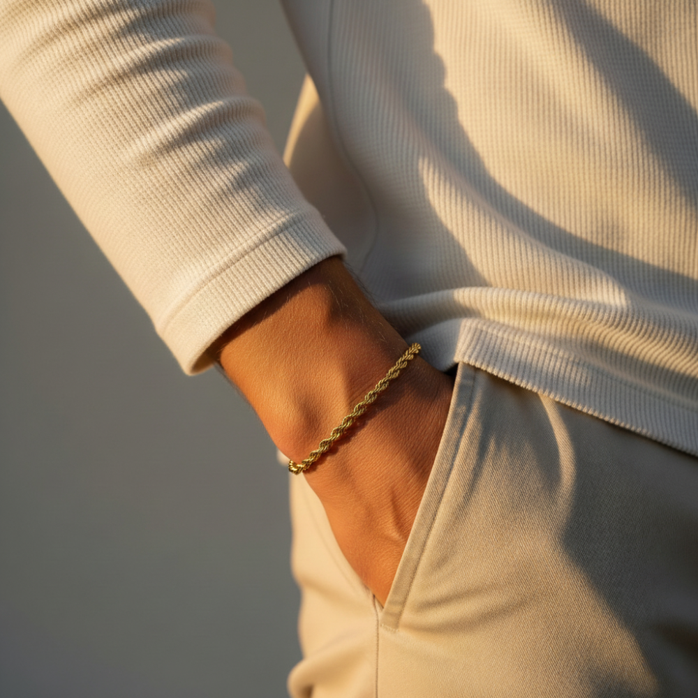 Close-up of a person wearing a gold rope bracelet on a neutral background