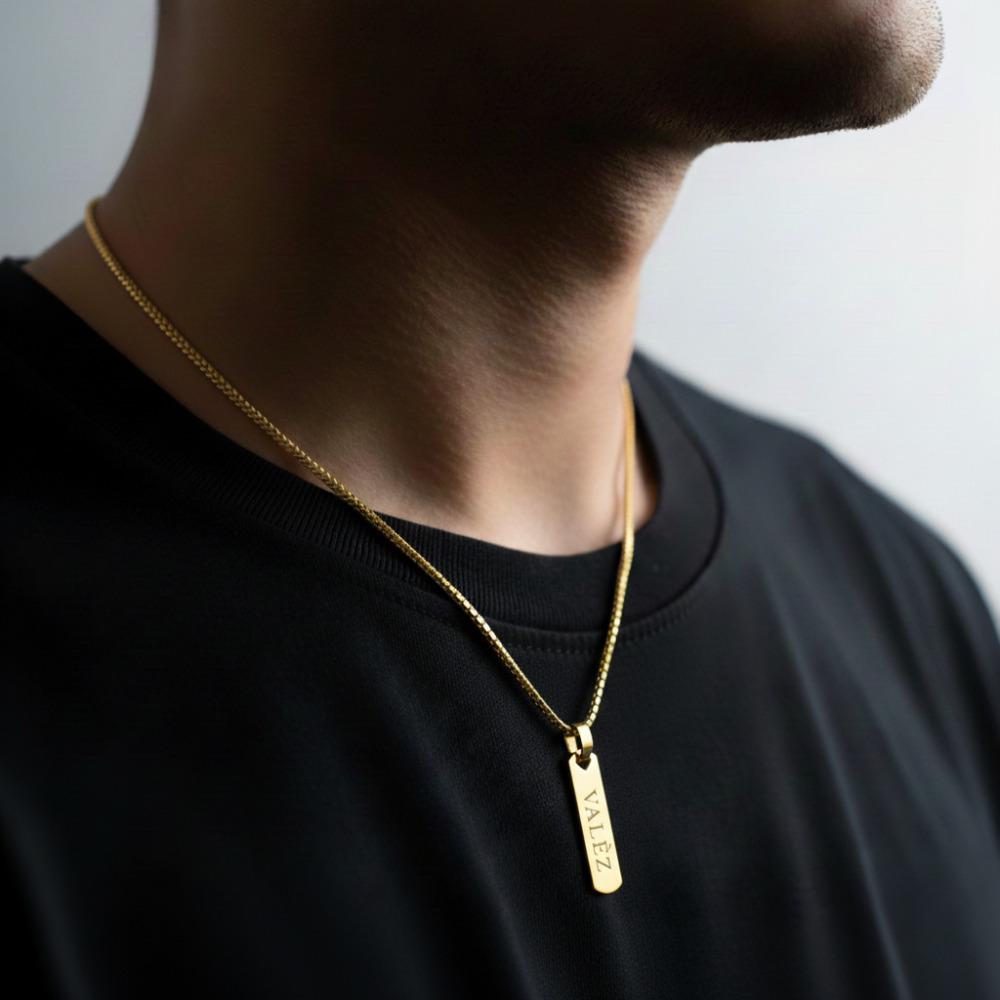 Person wearing a gold necklace with a pendant on a plain background