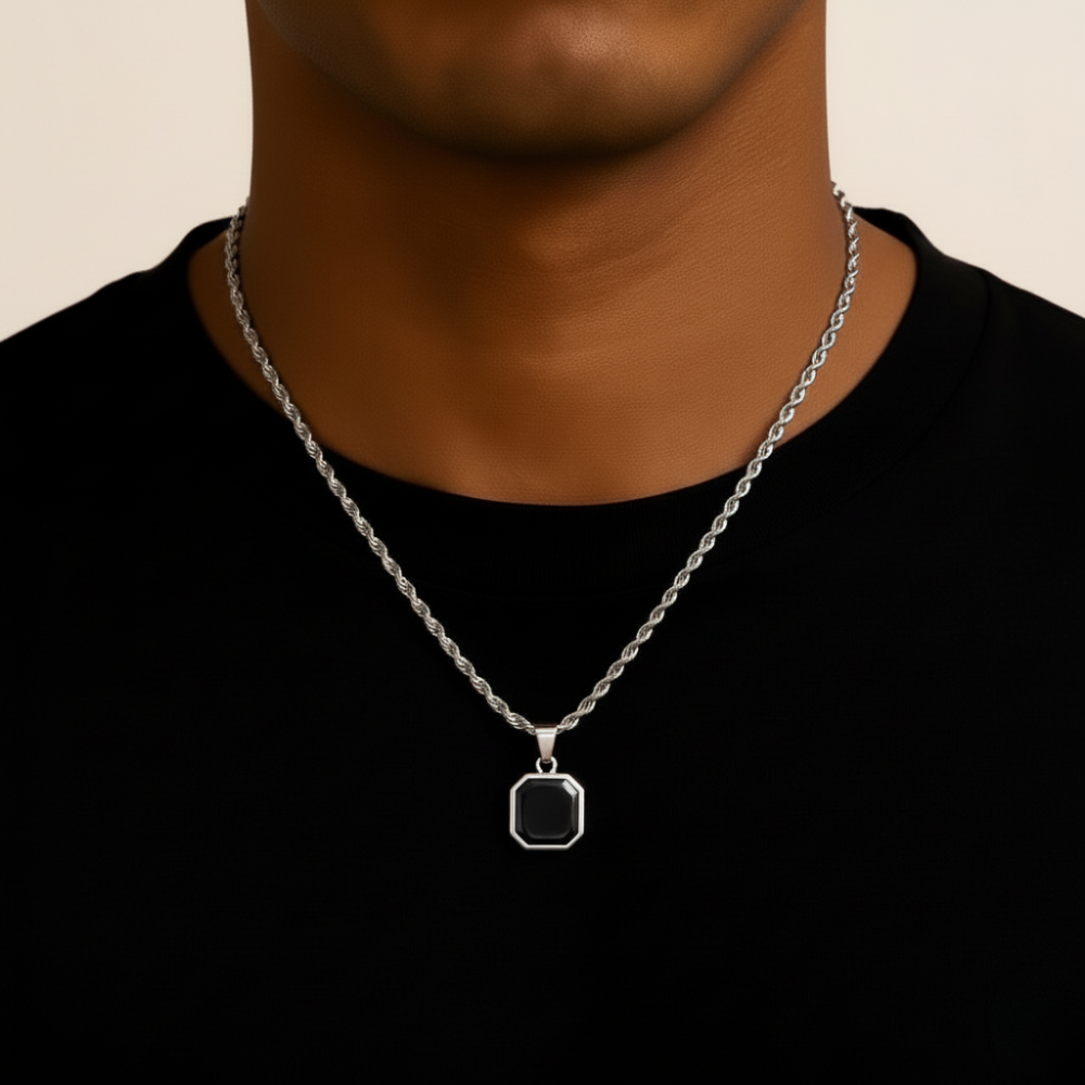Person wearing a stainless steel necklace with a black pendant on a beige background
