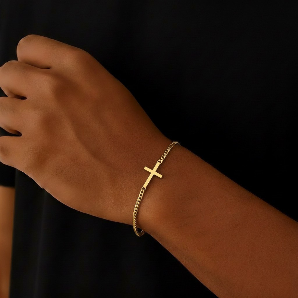 Gold cross bracelet on a wrist against a black background
