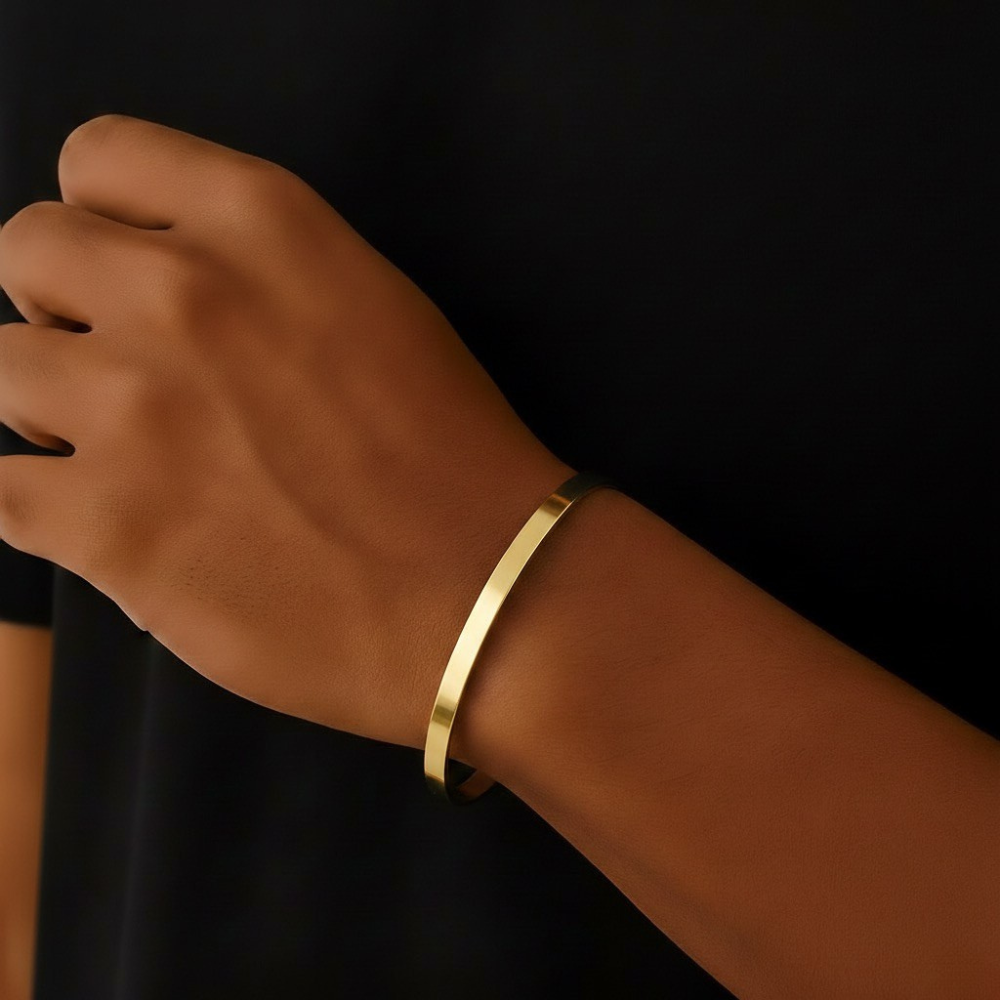 Gold bracelet on a wrist against a black background