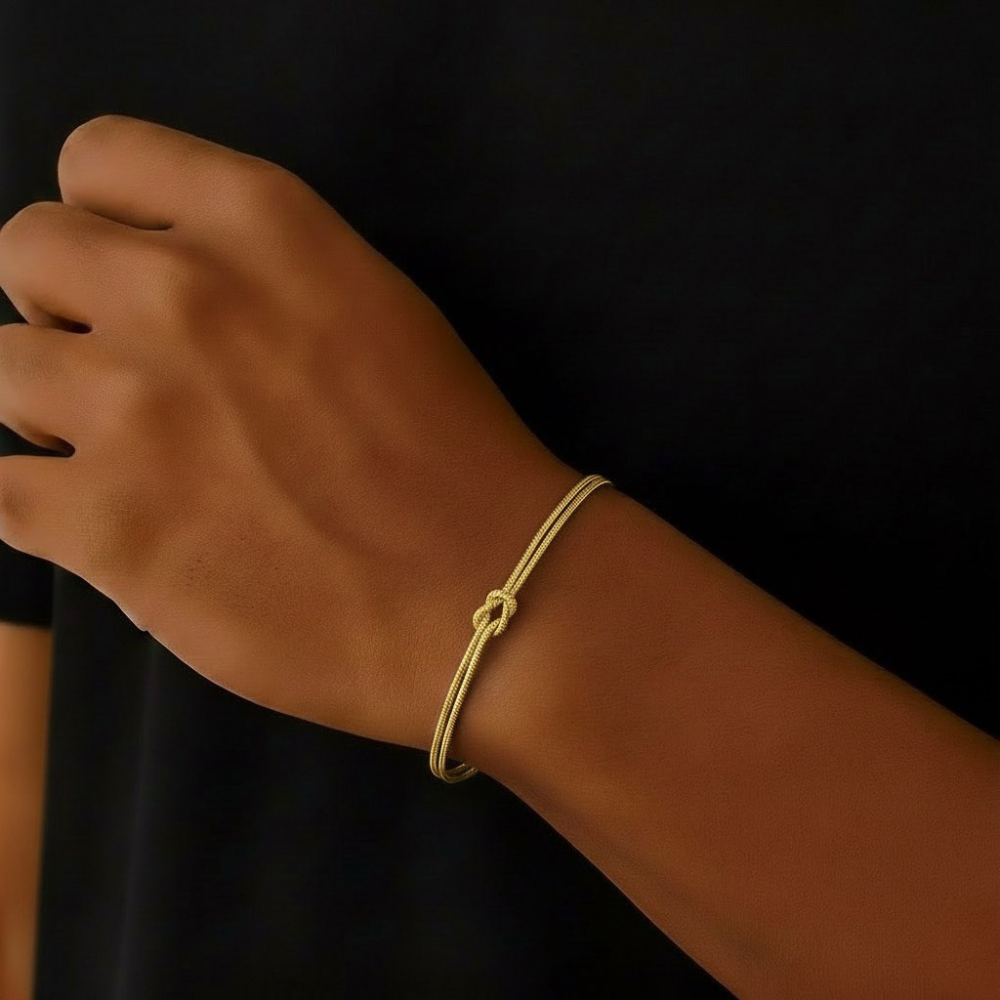 Gold Infinity bracelet on a wrist against a black background