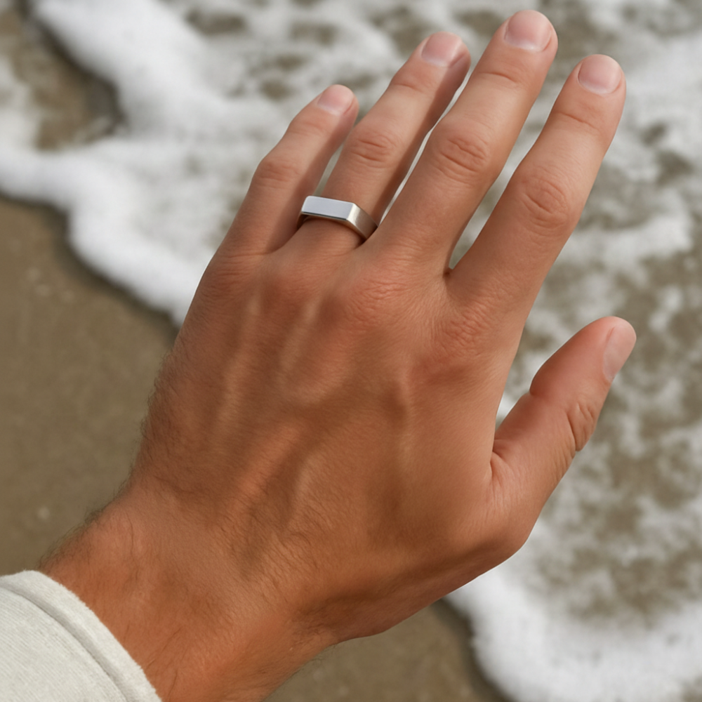 Hand wearing a silver ring with a beach background
