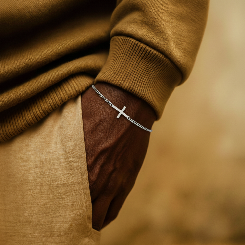 Close-up of a person wearing a brown sweater and beige pants with a silver cross bracelet featuring a cross design.